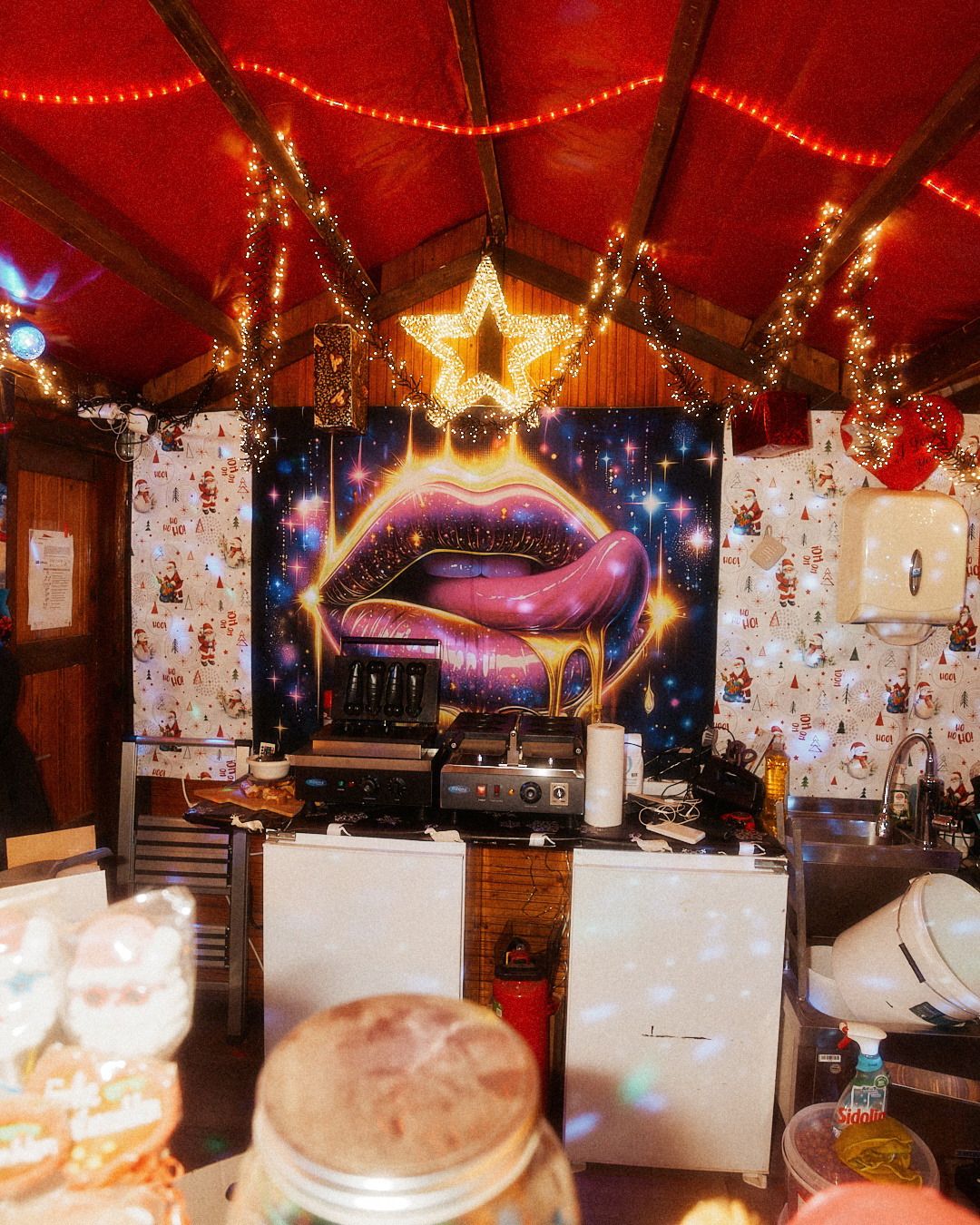 Ein Verkaufsstand auf einem Weihnachtsmarkt mit farbenfroher Dekoration und Imbiss-Zubereitung für die Besucher.