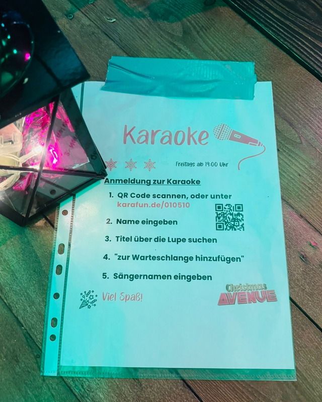 Eine Anleitung für die Karaoke-Teilnahme auf einem Schild bei der Christmas Avenue mit einer dekorativen Lampe daneben.