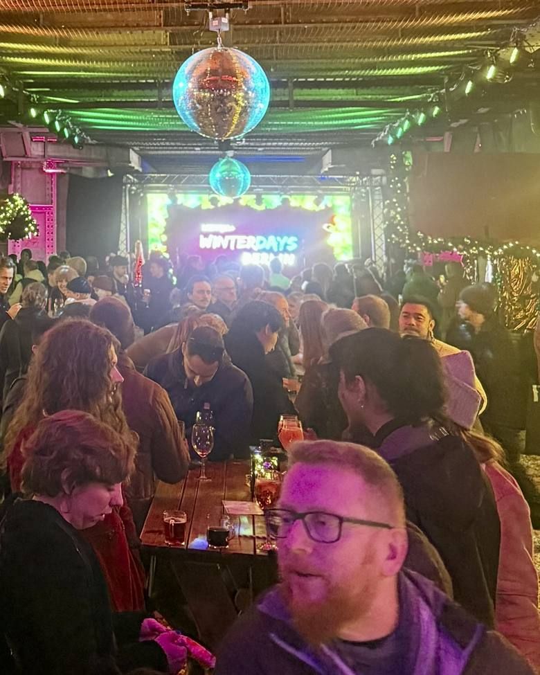 Menschen unter leuchtenden Discokugeln stehen bei festlicher Beleuchtung an einem Holztisch und trinken gemeinsam in einer Bar.