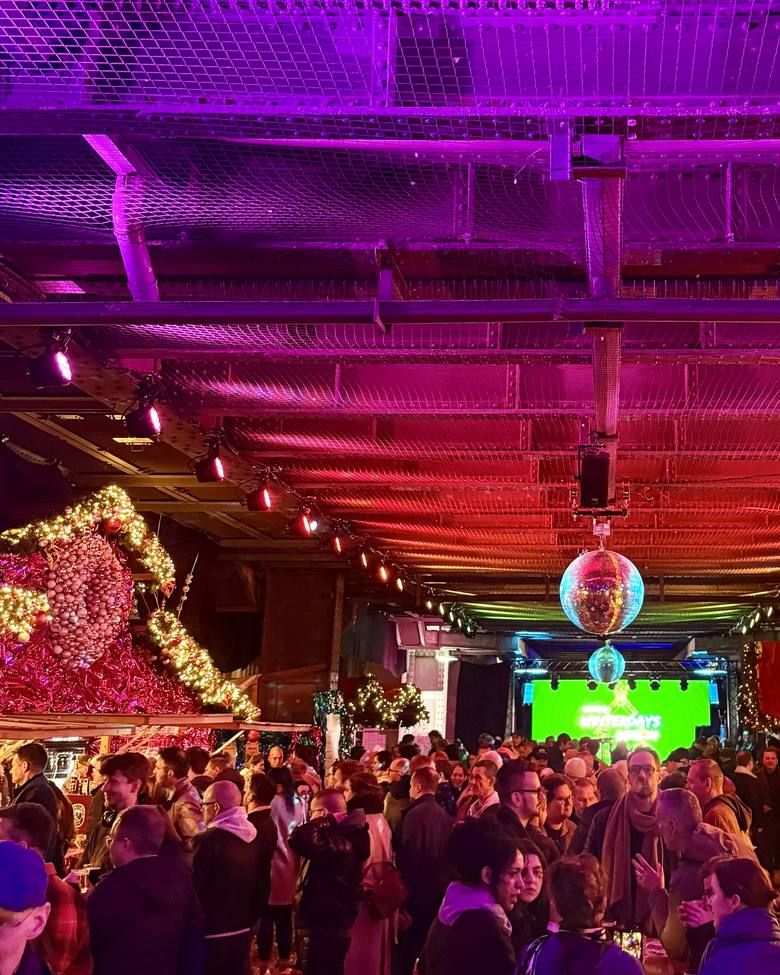 Zahlreiche Menschen unter einer festlich beleuchteten Decke mit Discokugeln bei einer gut besuchten Veranstaltung mit grüner Bühnenbeleuchtung.