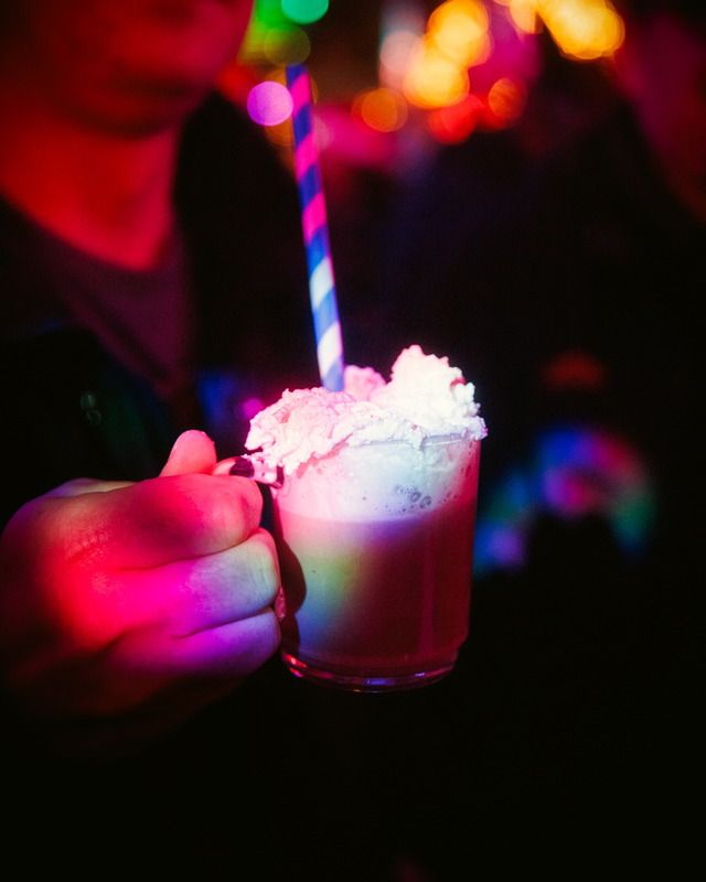 Ein Besucher hält eine Tasse mit heißem Getränk und Schlagsahne in einer atmosphärisch bunt beleuchteten Umgebung fest.