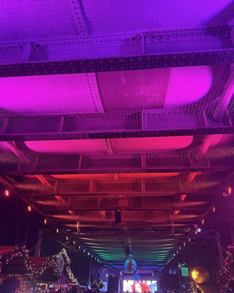 Bunte LED-Beleuchtung erhellt die industrielle Deckenkonstruktion einer festlich geschmückten Location mit einer hängenden Discokugel über den Besuchern.