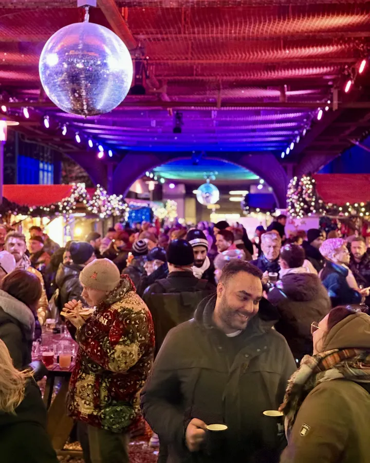 Zwei Gäste mit Glühweintassen an einem Tisch, hinter ihnen die volle Avenue und eine grosse Discokugel