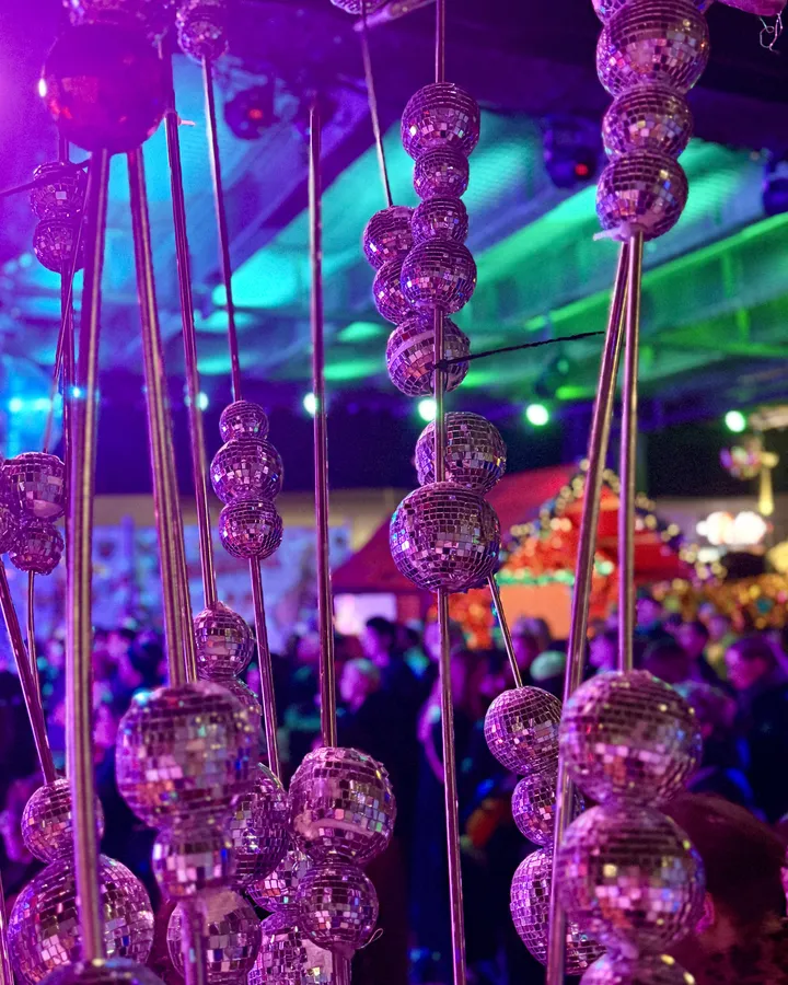 Reihen kleiner Discokugeln hängen an Stangen von der Decke, violett angeleuchtet