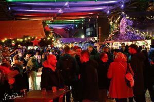 Besucher*innen genießen die festliche Stimmung auf der Christmas Avenue in Berlin, umgeben von beleuchteten Weihnachtsständen und Lichterketten