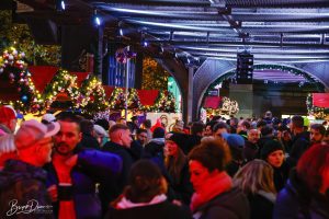Besucher*innen auf der Christmas Avenue in Berlin, umgeben von festlicher Beleuchtung und dekorierten Ständen unter der Hochbahn