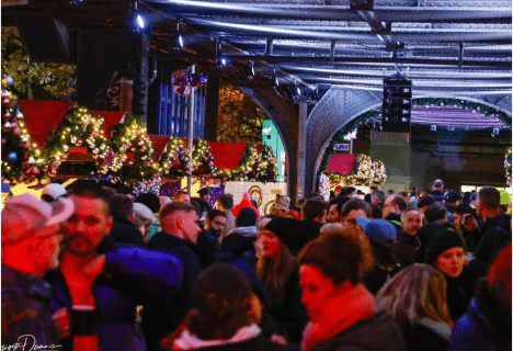 christmas-avenue-berlin-lgbtqia-weihnachtsmarkt.jpg Bunt beleuchteter LGBTQIA* Weihnachtsmarkt Christmas Avenue in Berlin, festliche Stände unter der Hochbahn mit einer fröhlichen Menschenmenge